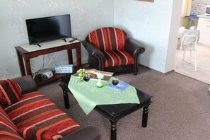 A living room with a sofa, armchair, coffee table, television, and a small table with a remote control. - Holiday apartment with 1 bedroom (Sassnitz)