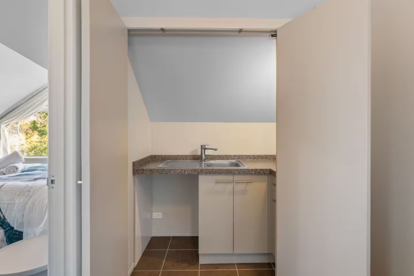A compact kitchen with a sink, cabinets, and a window overlooking a garden.