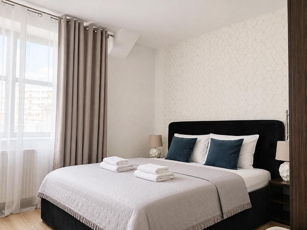 A hotel room with a bed, curtains, a nightstand, and a lamp.