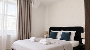 A hotel room with a bed, curtains, a nightstand, and a lamp.