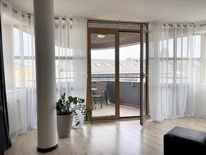 Habitación con puerta de cristal corredera que da a un balcón exterior. Hay una planta en maceta en el suelo.