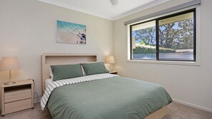 A bedroom with a bed, bedside tables, a window with a view of trees, and a painting on the wall. - Moola Haven – Hawks Nest (Hawks Nest)