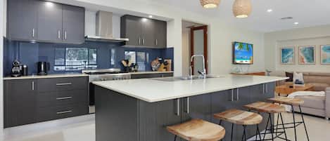 A modern kitchen with a large island, bar stools, and a dining area with a sofa.