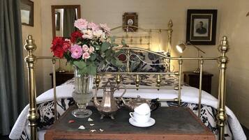 A bed with a metal frame, a vintage suitcase, a teapot, a cup, and a vase with flowers.
