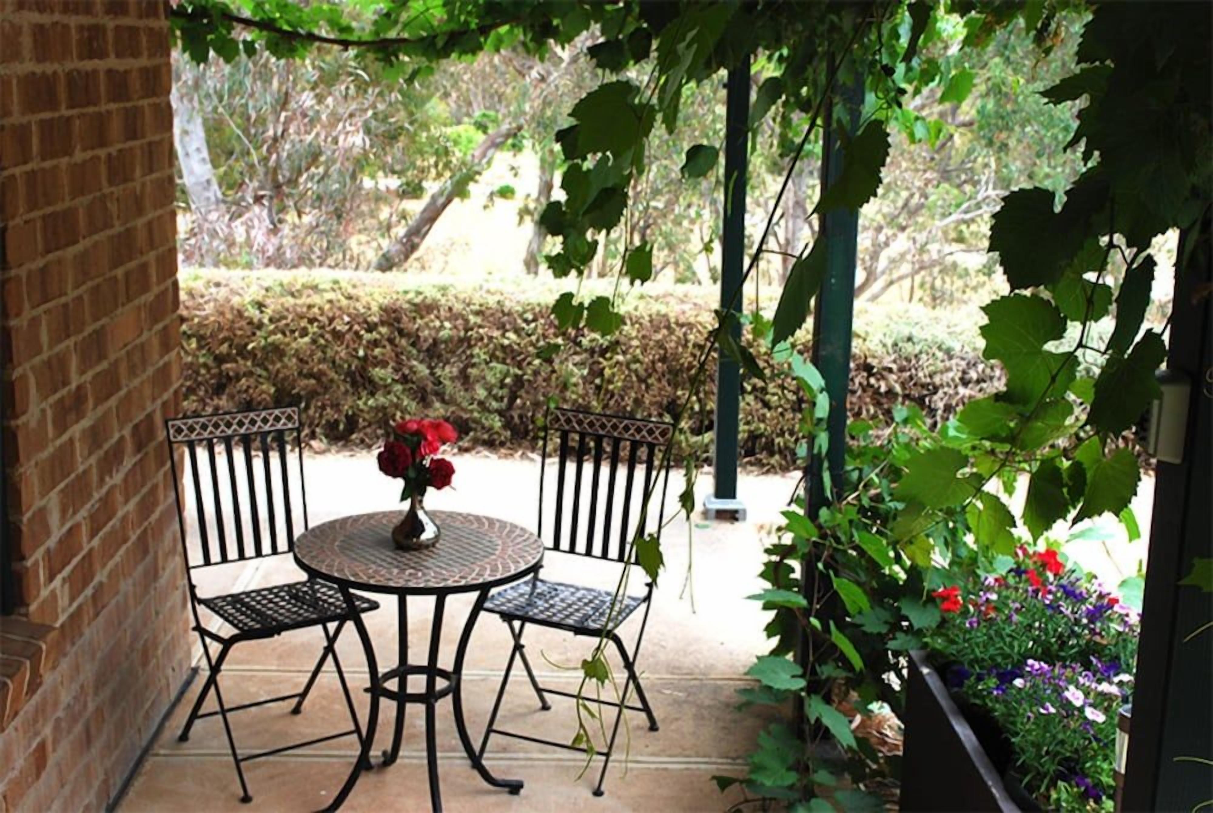 A patio with a round table and four chairs, surrounded by greenery and a brick wall.