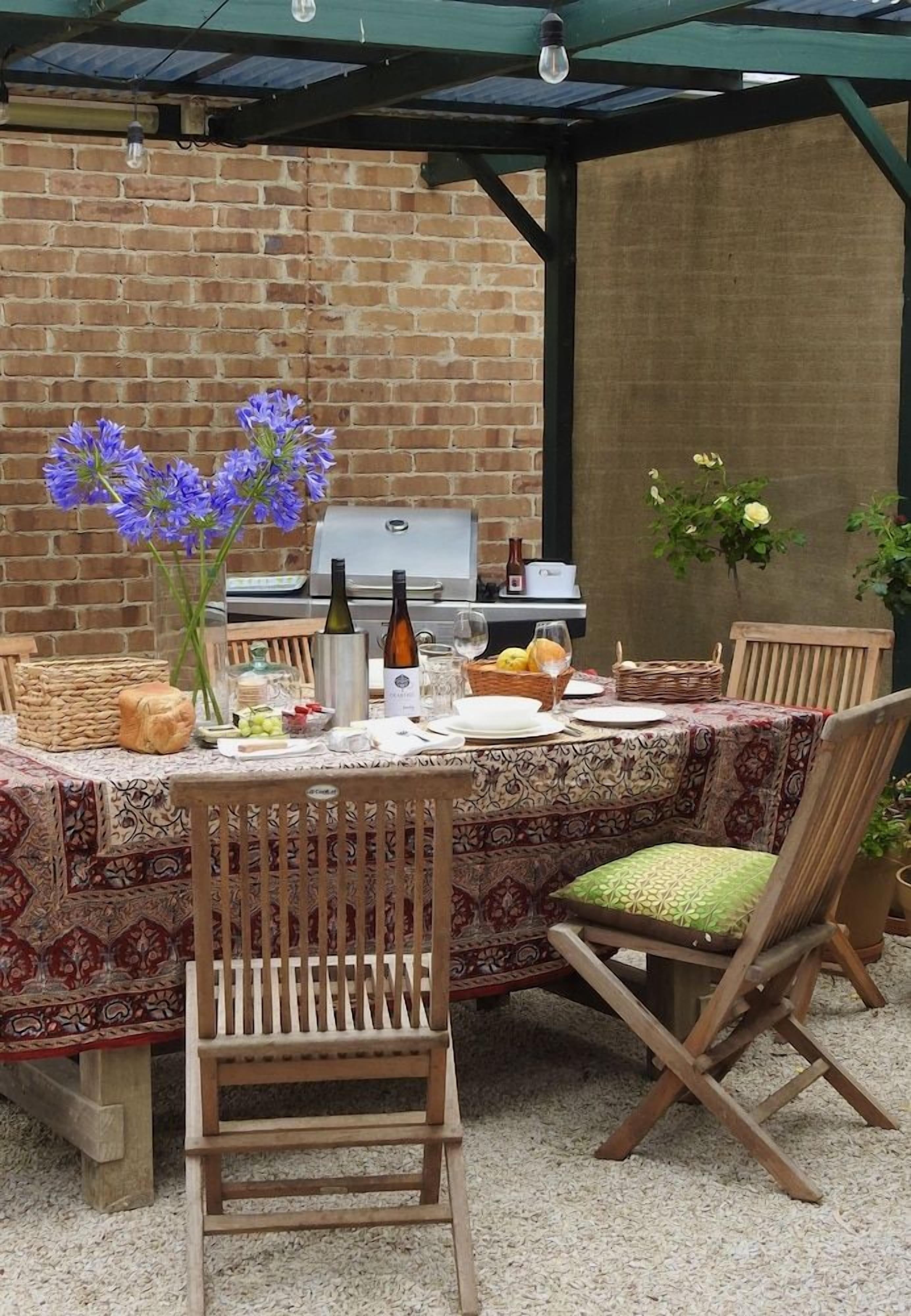 An outdoor dining area with a brick wall, a grill, and a table set with plates, glasses, and flowers.