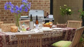 An outdoor dining area with a brick wall, a grill, and a table set with plates, glasses, and flowers.