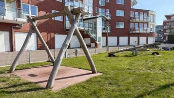 A playground with a swing set and a slide in front of a multi-story building with balconies.