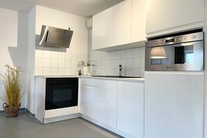 Eine moderne Küche mit weißen Schränken, einem eingebauten Backofen, einer Mikrowelle und einer Edelstahl-Dunstabzugshaube.