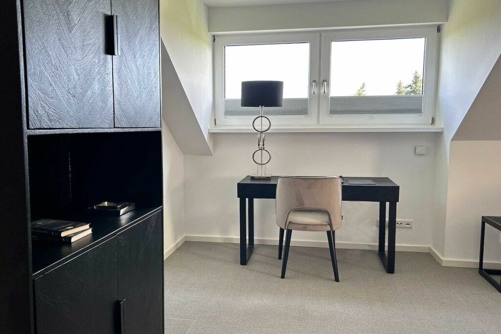Een kamer met een bureau, stoel en een raam met zonwering.