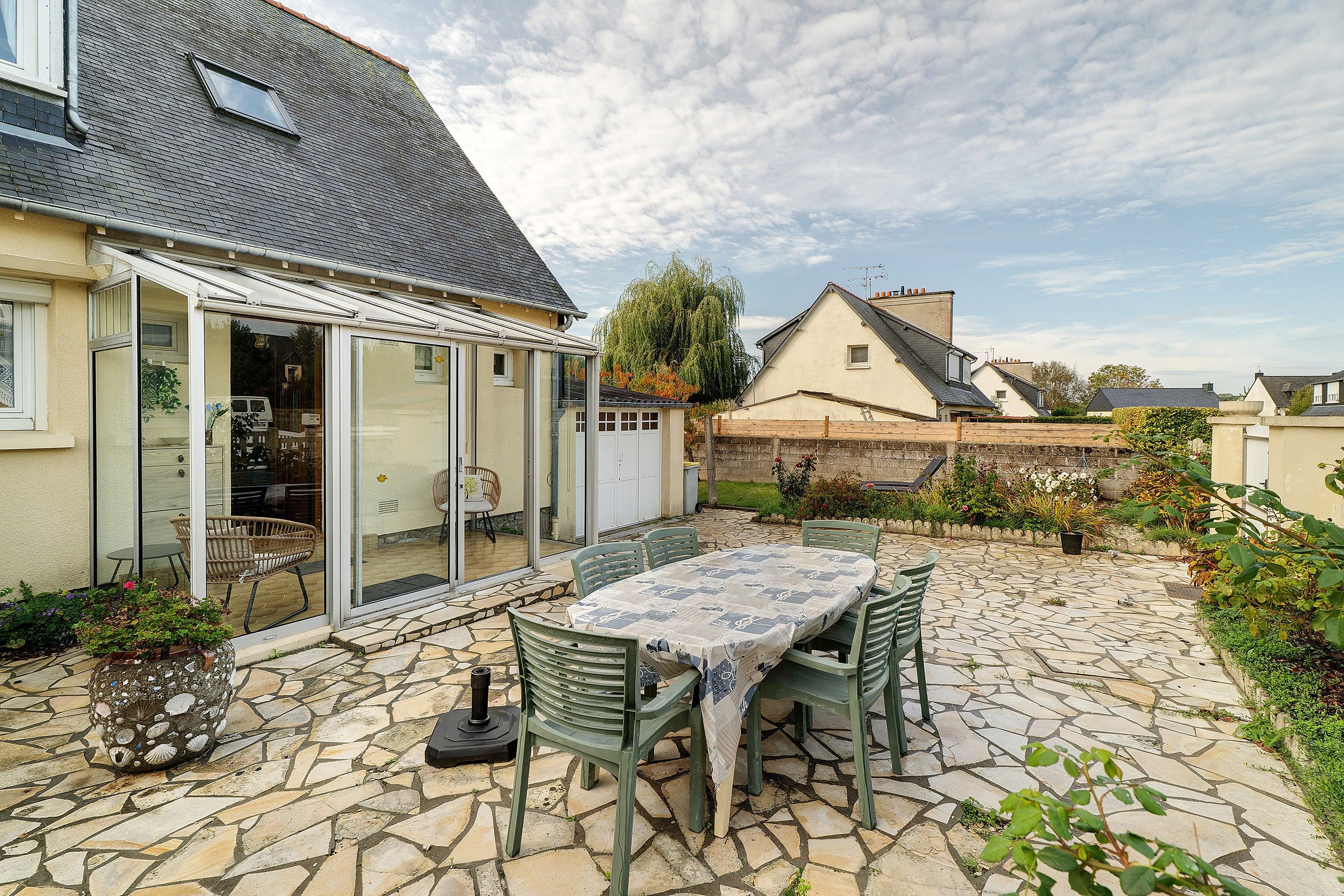 A patio with a table and chairs, a glass door entrance, and a stone-tiled floor.
