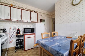 Eine kompakte Küche mit weißen Schränken, einer Mikrowelle, einem Kühlschrank und einem Esstisch mit Stühlen.