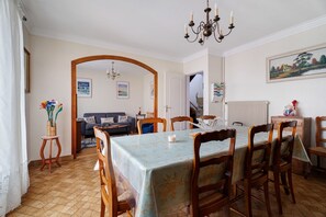 Ein Essbereich mit einem Tisch, der für sechs Personen gedeckt ist, umrahmt von Holzstühlen. Eine Pendelleuchte hängt von der Decke, und ein Gemälde ziert die Wand.