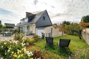 A house with a sloped roof, a covered patio, and a garden with flowers and chairs. - Chez Monique: family house in Saint Coulomb near beaches (Saint-Coulomb)