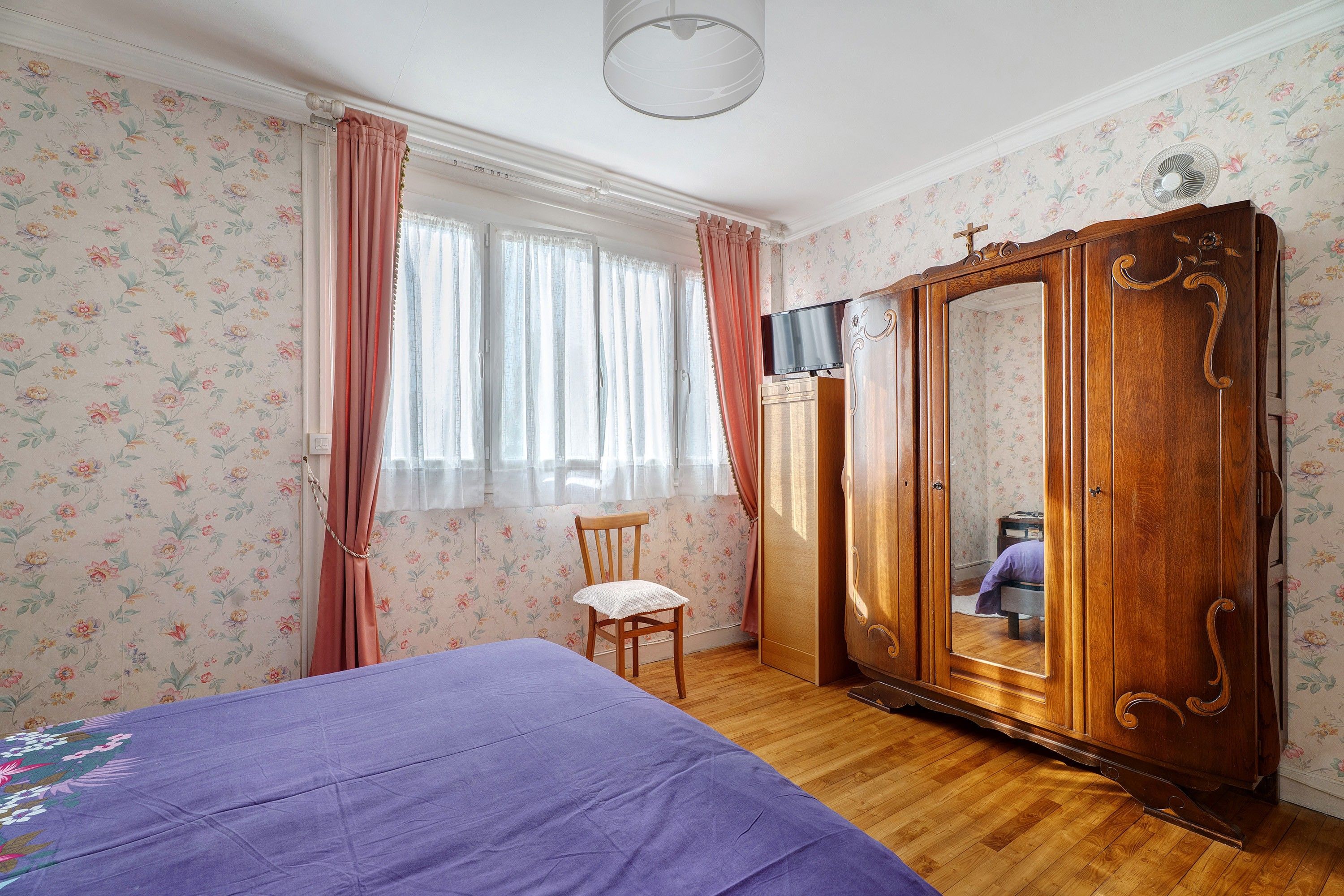 A bedroom with a bed, a wooden wardrobe, a chair, and a television.