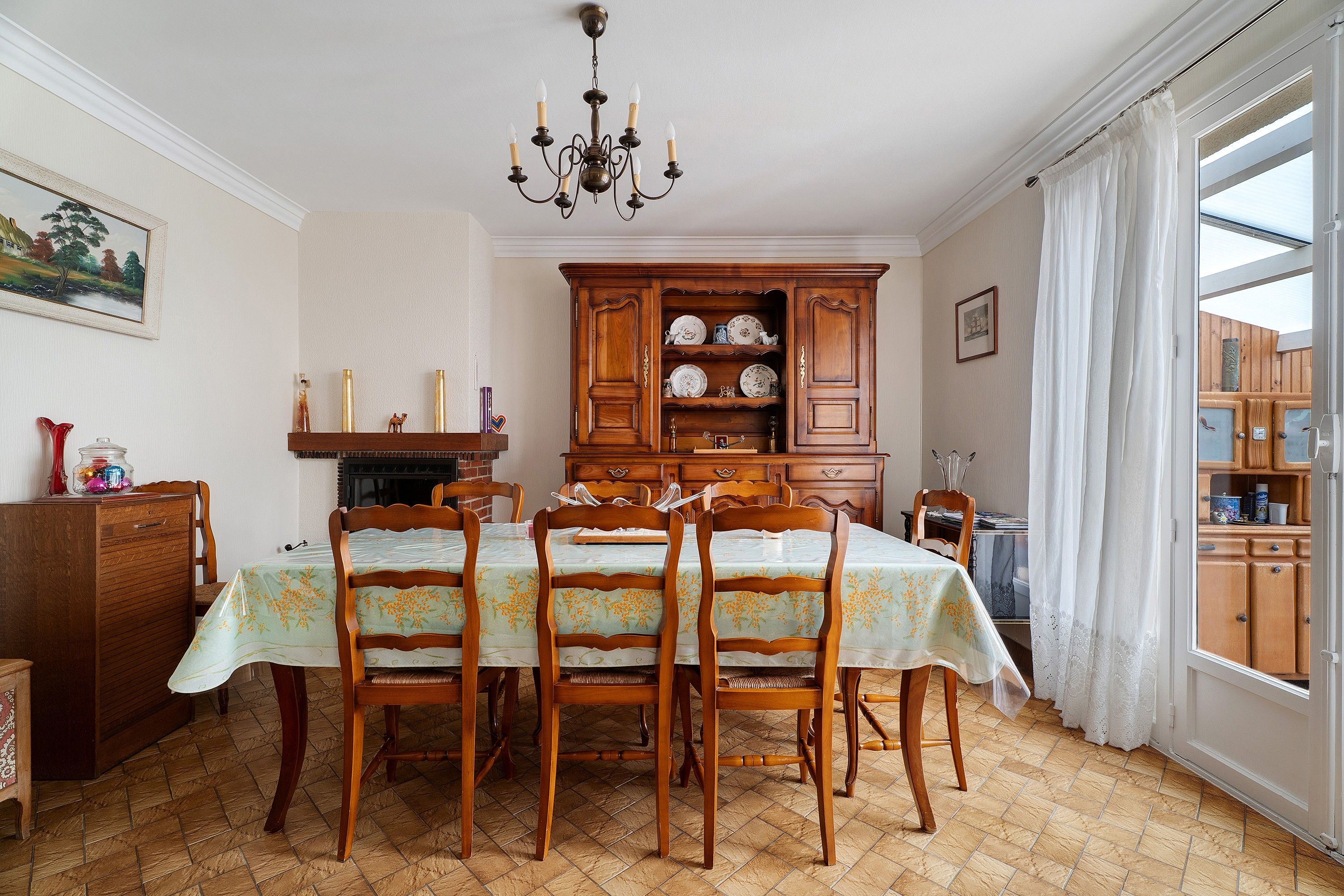 Ein Esszimmer mit Tisch für vier Personen, Holzkästen, einem Chandelier, einem Serverschrank mit Geschirr und einem Gemälde an der Wand.