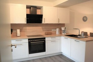 A modern kitchen with white cabinets, a built-in oven, a coffee maker, and a sink. - House No. 26, Holiday Home Fischerhus (Wangerland)