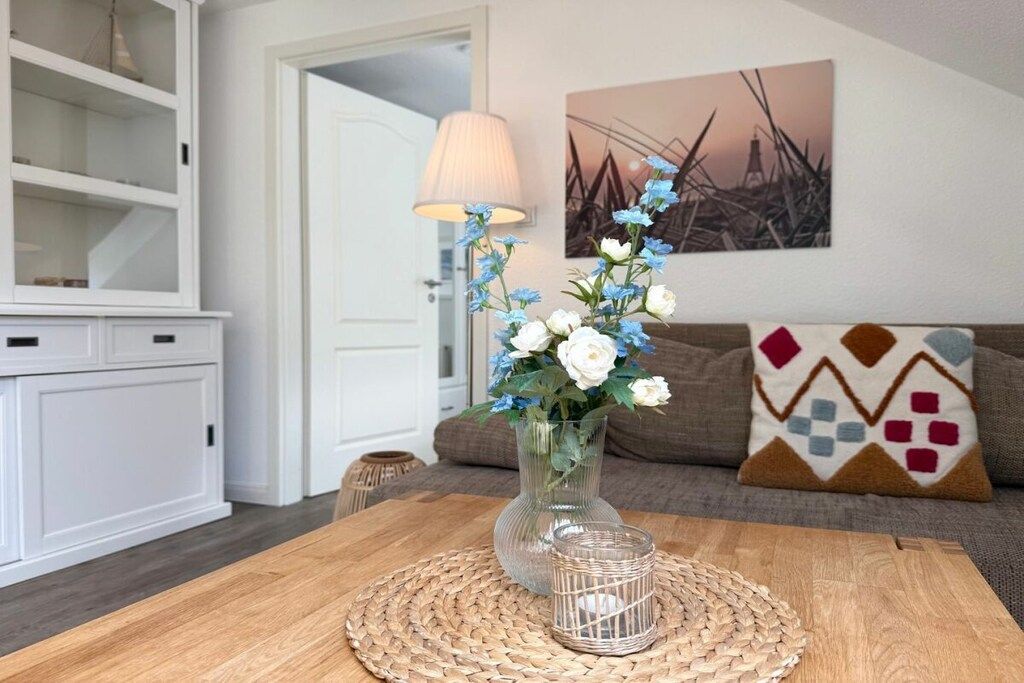 A dining area with a wooden table, a woven placemat, a clear glass vase with flowers, a lamp, and a painting on the wall.