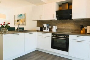 A modern kitchen with white cabinets, a built-in oven, a coffee maker, and a sink. - House No. 19, Fischerhus (Wangerland)