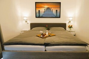 Uma cama com uma bandeja de itens de café da manhã, uma pintura de um cais e duas luminárias de parede.