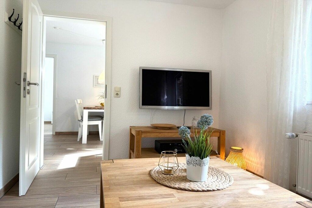 Ein Zimmer mit einem Holztisch, einem flachbildfernseher an der Wand und einem Blumentopf auf dem Tisch.