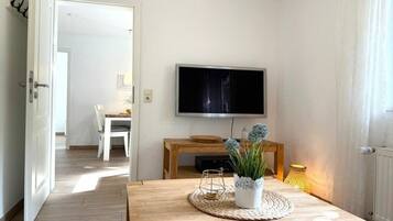 Ein Zimmer mit einem Holztisch, einem flachbildfernseher an der Wand und einem Blumentopf auf dem Tisch.