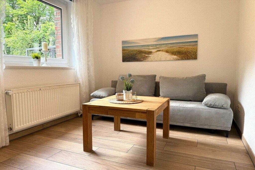 Ein Wohnzimmer mit einer Couch, einem Holztisch, einem Fenster mit Blick auf Bäume und einem Gemälde an der Wand.