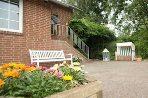 Ein Backsteinhaus mit einer weißen Bank und Blumenbeeten im Vordergrund.