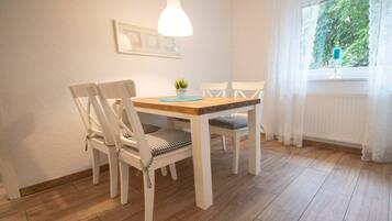 A dining area with a wooden table and white chairs, a pendant light, and a window with curtains.