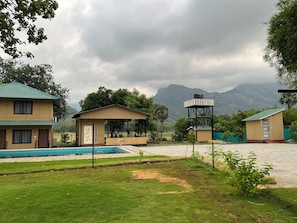 A hotel with a swimming pool, a covered seating area, and a view of mountains.