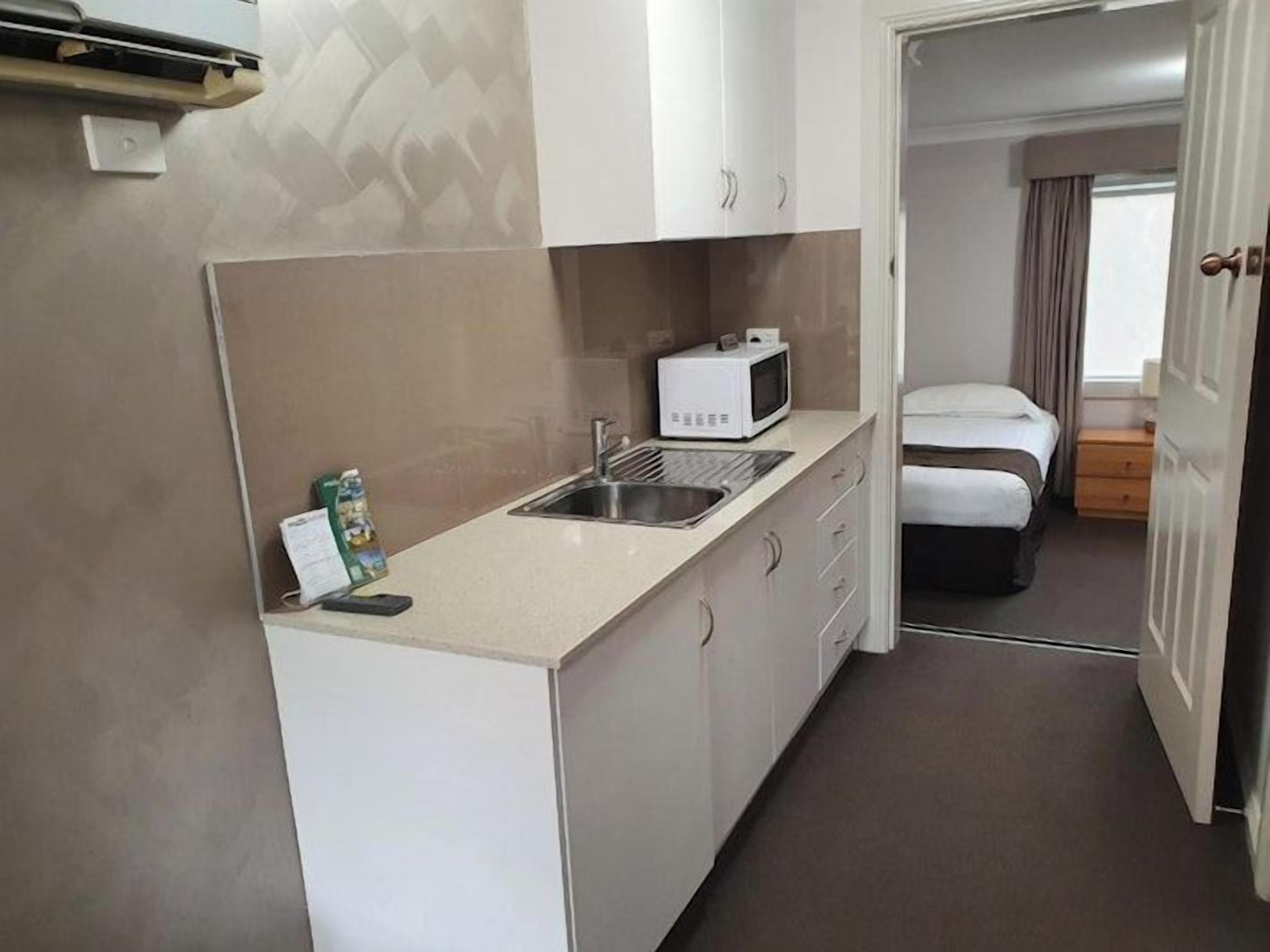 A compact kitchenette with a microwave, sink, and cabinets.