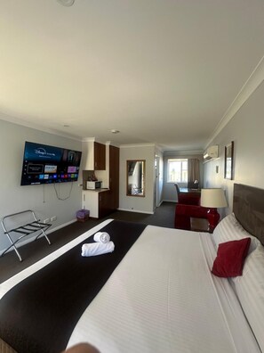 Habitación de hotel con cama, televisor montado en la pared, escritorio con silla y espejo.