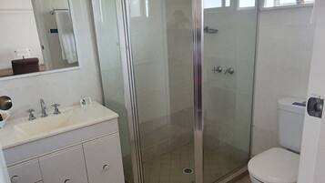 A bathroom with a glass-enclosed shower, a white sink with a mirror above it, and a toilet.