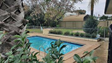 A swimming pool surrounded by a fenced garden with various plants and trees.