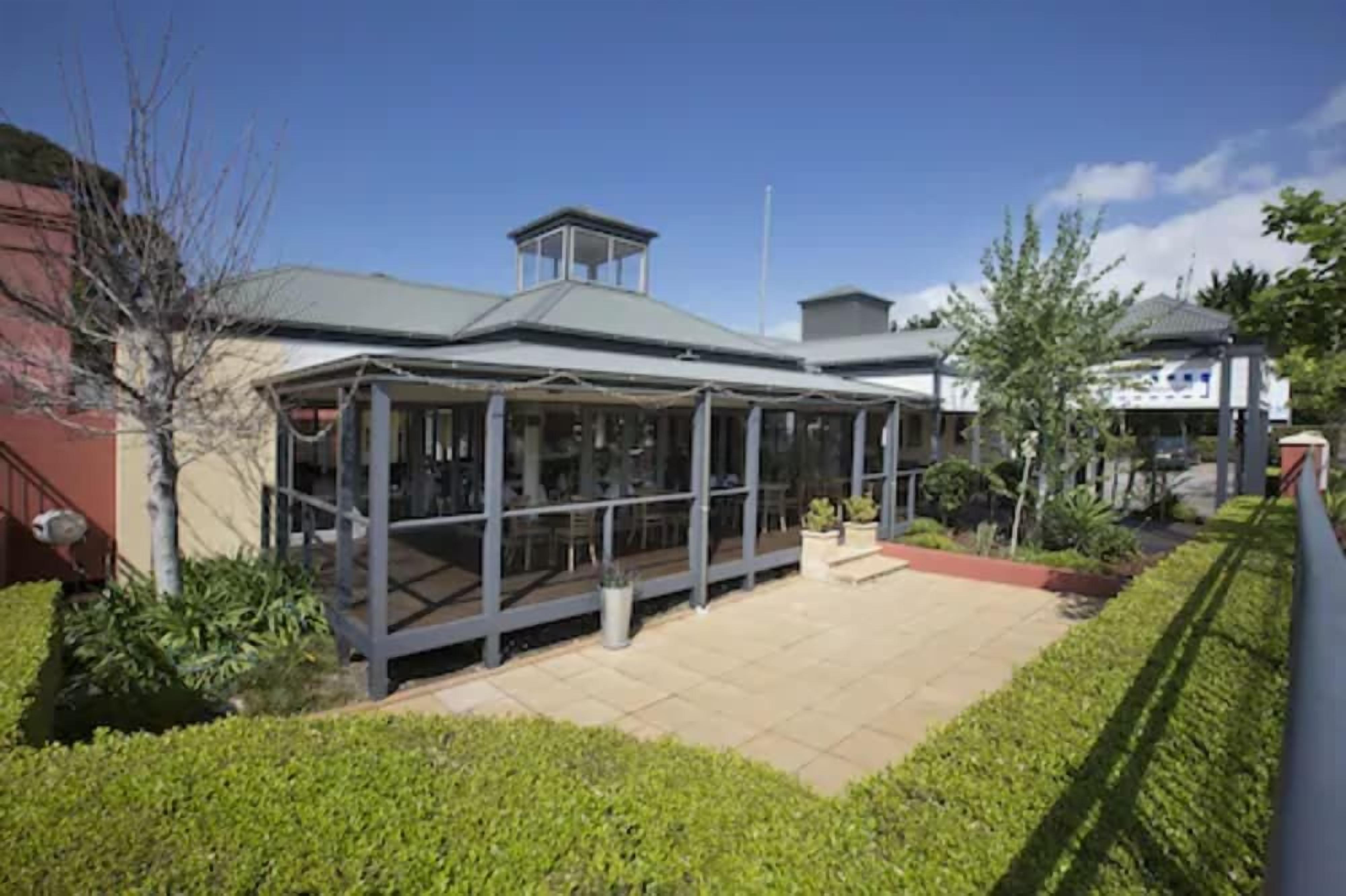 A modern building with a glass enclosure, a covered outdoor area, and a clear sky.