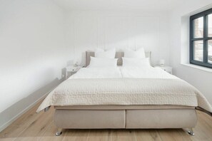 A bedroom with a bed, nightstands, and a window. - Coastal Suite South | Side Waterfront Location (Greetsiel, Germany)