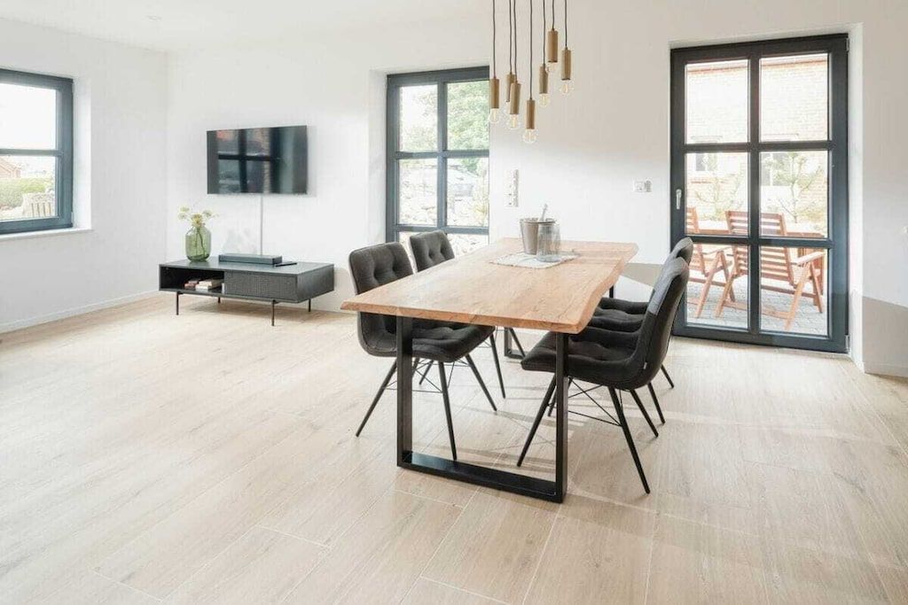 A modern dining area with a wooden table, black chairs, a TV mounted on the wall, and a large window with a view.