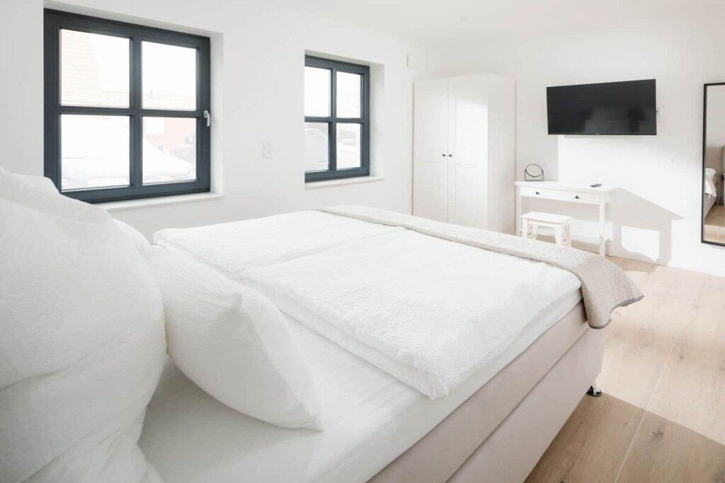 Ein Schlafzimmer mit einem Bett, einem Schreibtisch, einem Sessel, einem Kleiderschrank und einem an der Wand befestigten Fernseher.