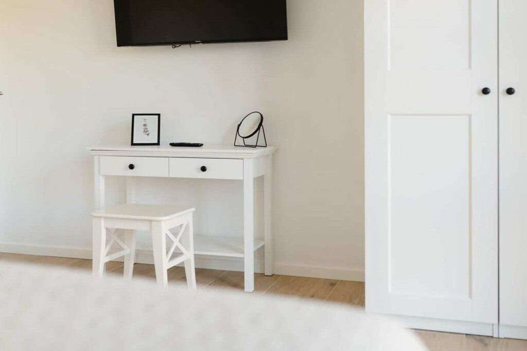 Un bureau blanc avec une chaise, un tableau encadré et un miroir.