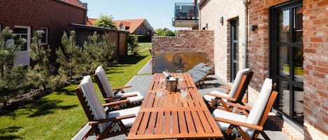 An outdoor patio with a wooden table and chairs, a brick wall, and a clear sky.