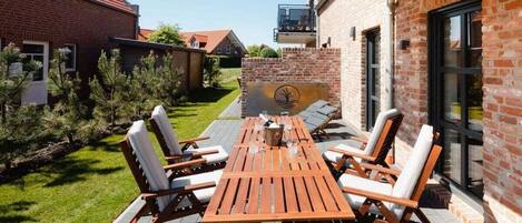 Un patio exterior con una mesa y sillas de madera, rodeado de muros de ladrillo y una zona ajardinada.