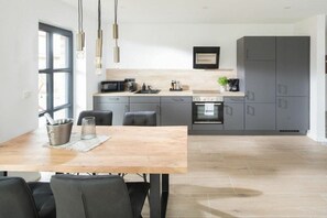 A modern kitchen with grey cabinets, a wooden dining table, and pendant lights. - Coastal Suite South | Side Waterfront Location (Greetsiel, Germany)
