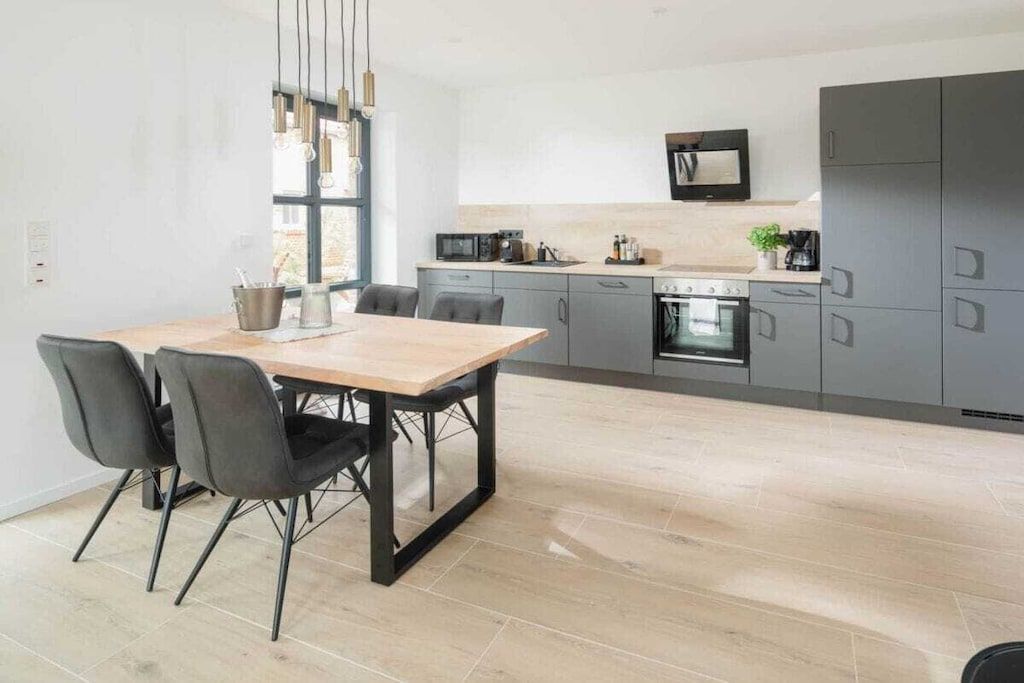 A modern kitchen with grey cabinets, a wooden dining table, and black chairs.