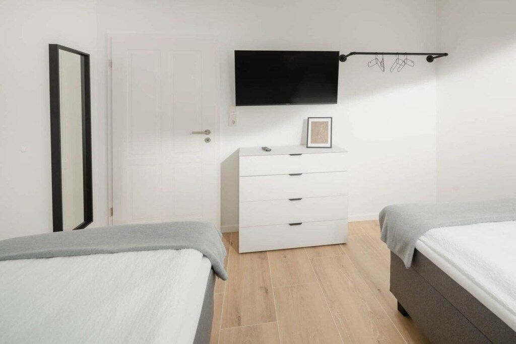 Un dormitorio con dos camas, un aparador blanco, un televisor de pantalla plana en la pared y una puerta.