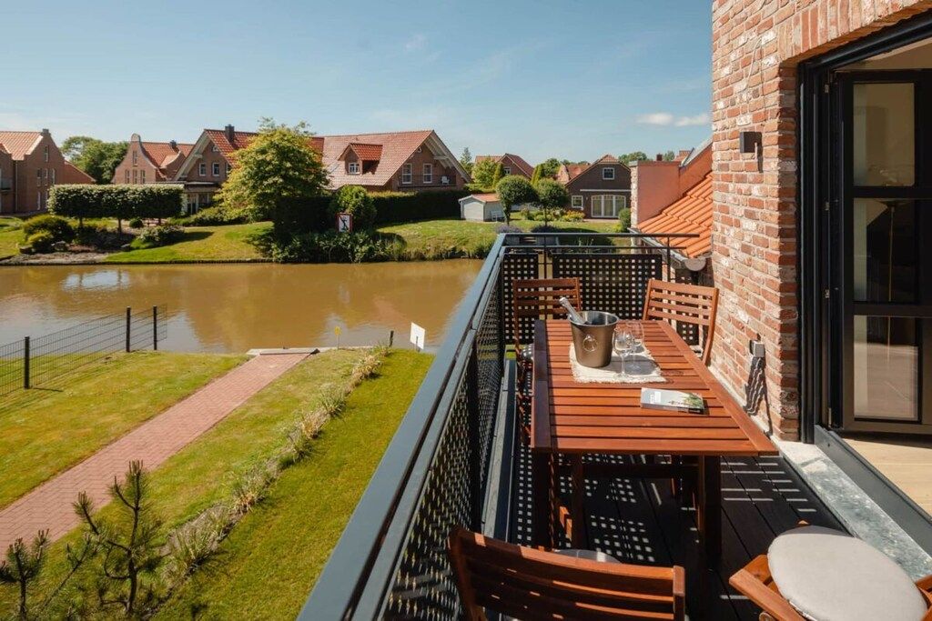 A balcony with a table and chairs overlooking a river and residential buildings.