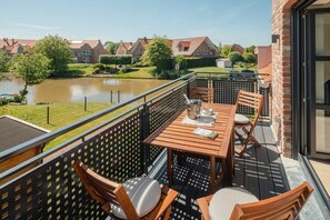 Ein Balkon mit Holztisch und -stühlen, Blick auf einen Fluss, und eine Häuserreihe im Hintergrund.