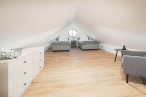 A spacious attic bedroom with a high ceiling, two beds, a small table, and a window. - Coastal Suite East | Directly on the waterfront (Greetsiel)