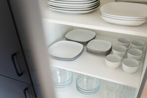 Un armario de cocina con platos, tazones y tazas blancos ordenados en estantes.