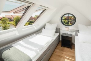 A bedroom with a skylight, a round mirror, and a view of a garden. - Coastal Suite East | Directly on the waterfront (Greetsiel)
