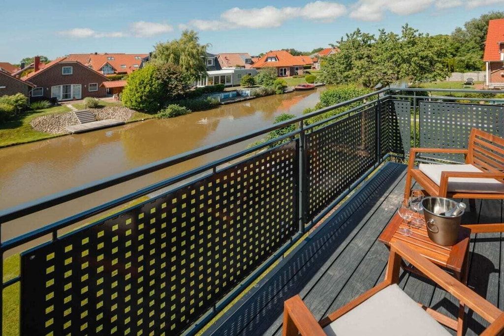 Un balcon donnant sur une rivière, avec des meubles en bois et une rambarde en métal.